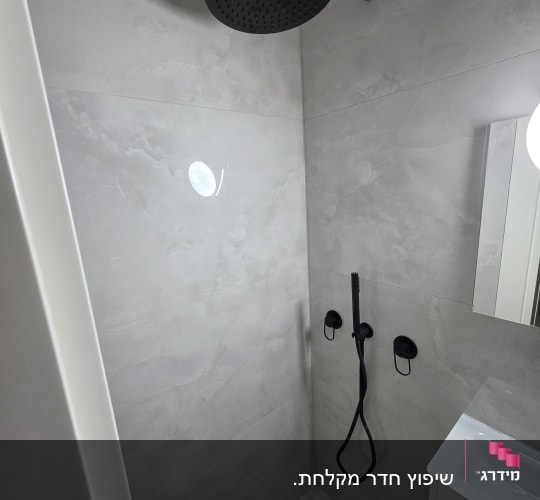 מקלחת עם ראש מקלחת שחור וקיר אריחים אפור